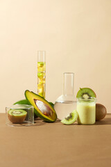 Laboratory glassware placed on brown surface with fresh kiwis and avocados. A beaker contains a mixture of avocado and kiwi featured. Science advertising laboratory background