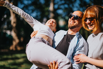 Young adults have fun in a park on a sunny day a man lifts a woman in joy, while another woman...