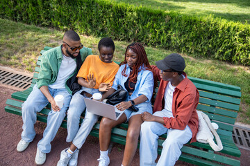Enthusiastic group of african american students stare into laptop screen sit on bench on university...