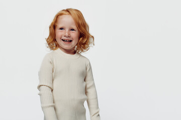 Little girl with red hair in white sweater and blue jeans, fashion portrait of a young child beauty