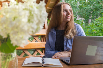 Young woman freelancer working online using laptop and enjoying the beautiful nature outdoors in garden. Online meeting education. Worcation, work from vacation, hybrid work model