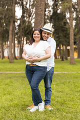 A man and woman are standing in a grassy field, smiling at the camera