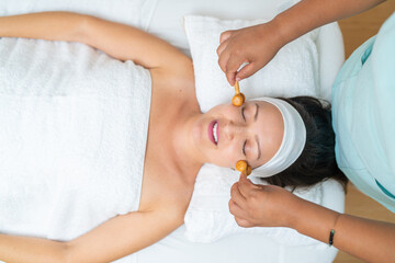 Woman enjoying facial massage with natural wood rollers in spa