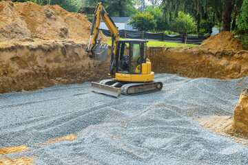 An excavator fills irregularities in excavations with granite rubble base to serve as foundation...
