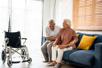 Asian active senior man support elderly woman from wheelchair to sofa.