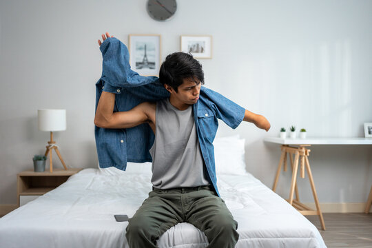 Asian young amputee without arm wearing a t-shirt while sitting on bed. 