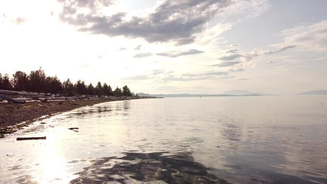 Low tracking shot over high tide debris with sunset reflection on calm Pacific Ocean near Comox BC Canada.
