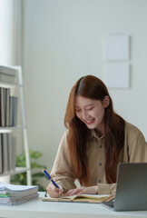 Young woman working on laptop in office Asian businesswoman sitting and taking notes in a notebook Thinking of ideas at your desk Beautiful independent woman working online with paperwork.