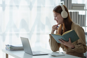 Young Asian woman looks happy wearing headphones Watch the webinar Listen to online courses...