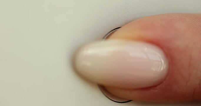 Closeup of a finger pressing power button on white electronic device.