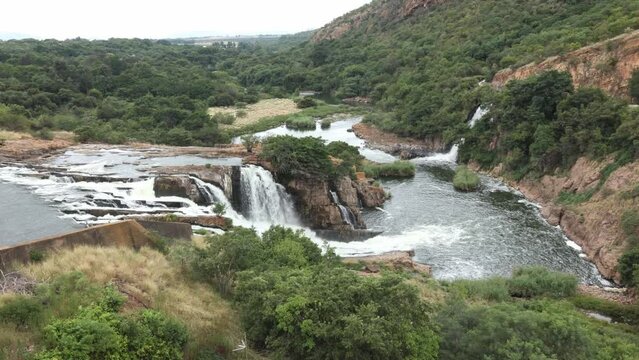 A landscape view of a set of waterfalls and cascades showing the terrain of rocky layers and forest vegetation on the downstream side of the Hartbeespoort dam wall in the Magaliesberg in South Africa.