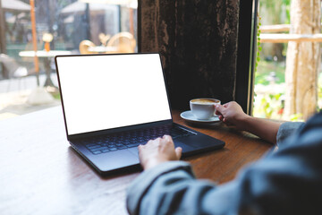 Mockup image of a woman working on laptop computer with blank white desktop screen while drinking coffee in cafe
