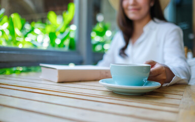 Closeup image of a woman drinking coffee with a book on table