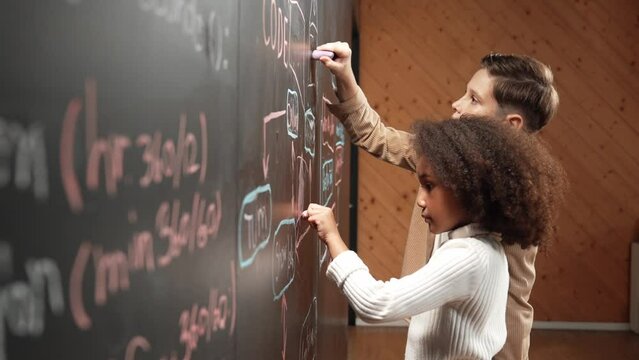 Diverse student brainstorm engineering prompt on blackboard. Group of happy children helping, support to create and design STEM technology classroom in casual cloth. Site view. Closeup. Erudition.