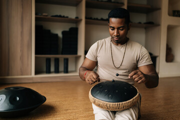 Portrait of relaxed African-African man in trance playing meditative instrument tank drum using...