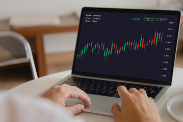 Person analyzing stock market data on laptop with candlestick chart, financial trading.