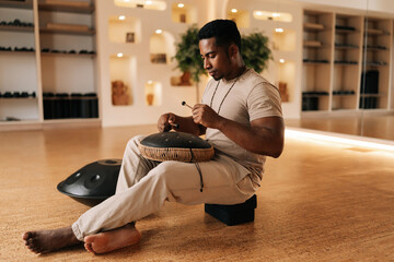 Happy calm black drummer male in trance enjoying playing using drumsticks on glucophone sitting...