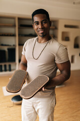 Vertical portrait of positive black male holding in hands wooden Sadhu Board with nails standing in...