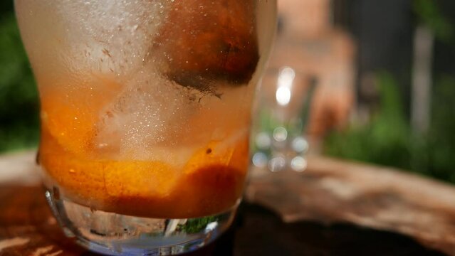 A close-up shot of a person muddling a Caipirinha cocktail with a wooden muddler. A tangerine Caipirinha being stirred on the table. Mixing a Caipirinha recipe: cacha&ccedil;a, tangerine, sugar and ice cubes