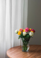 A bright bouquet of yellow, white, pink roses in a glass vase on a wooden table in the living room