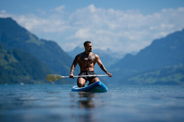 Male fit muscular model with paddle board. Guy paddling on paddleboard. Healthy summer lifestyle....