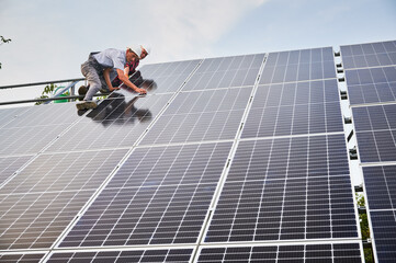 Male workers building photovoltaic solar panel system outdoors. Men installers placing solar module...