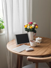 Home office - tablet, keyboard, cup of tea, bouquet of roses on a round wooden table in the living room