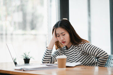 A woman is sitting at a desk with a laptop and a cup of coffee. She is looking at the laptop screen...