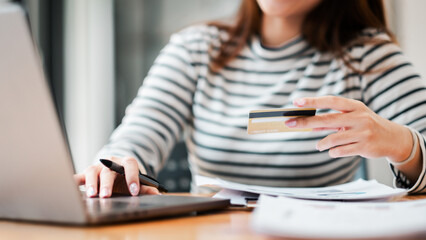 A woman is using a laptop to pay for something with a credit card. She is holding the card in her hand and she is focused on the task at hand