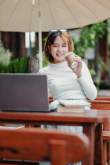 A woman is sitting at a table with a laptop and a cup of coffee. She is smiling and she is enjoying her time