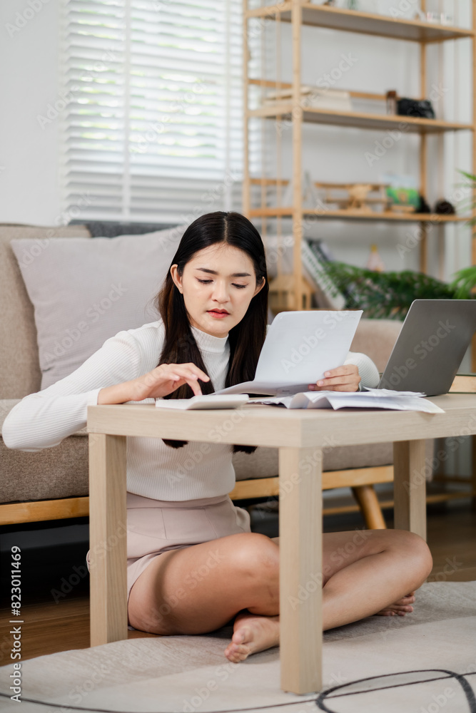 Poster a woman is sitting on the floor in front of a table with a laptop and a stack of papers. she is focu