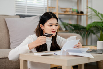 A woman is sitting at a table with a credit card in her hand and a receipt in front of her. She looks worried and is checking the receipt