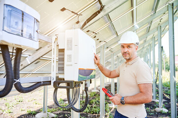 Professional worker checking voltage on solar inverter. Male using current probe to measure output...