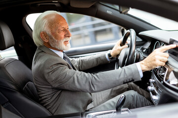 Elegant elderly gentleman drives luxury car through downtown streets