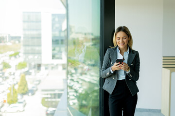 Smiling businesswoman talking on mobile phone by office window in daylight