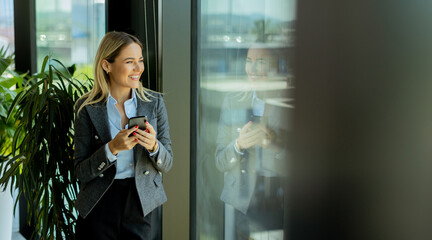 Smiling businesswoman talking on mobile phone by office window in daylight