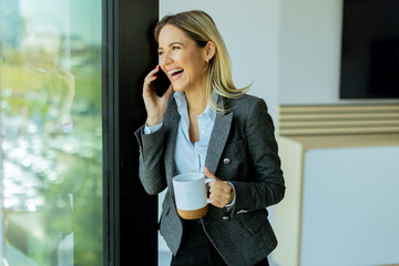 Businesswoman enjoying morning coffee and phone call in bright office