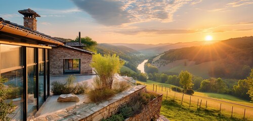 A luxury villa with a rustic stone exterior and modern glass additions, overlooking a secluded valley with rolling hills and a river, captured during a serene sunset. 