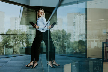 Confident businesswoman holding digital tablet while standing outside modern office building at noon