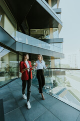 Two businesswomen discuss strategy outside modern office building in daylight