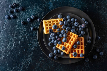 Belgian waffles with blueberries on a black plate.