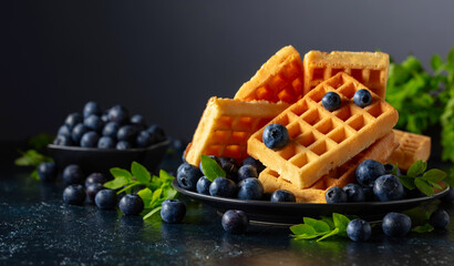 Belgian waffles with fresh blueberries on a black plate.