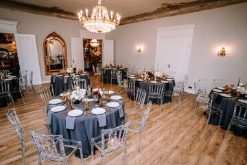 Riga, Latvia, - August 26, 2024 - a beautifully decorated event hall with elegant dining setups, including round tables covered in gray tablecloths, crystal clear chairs, and ornate chandeliers...