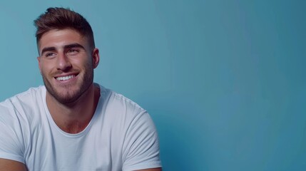 Fototapeta premium A man smiles at the camera, wearing a white T-shirt against a blue backdrop