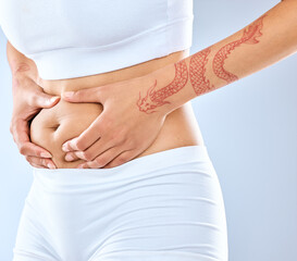 Woman, hands and belly with holding stomach for diet results isolated on studio background. Tattoo, fitness and abdomen with stubborn fat, cellulite and tummy tuck in sportswear for training