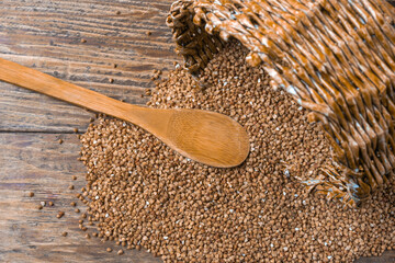 buckwheat groats and a wooden spoon are scattered on a wooden table , the concept of dietary...