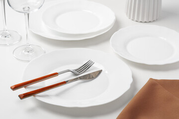 Stylish table setting with white dishware on white tablecloth