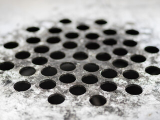 An aged ashtray metallic surface with grid-like patterns of circular holes