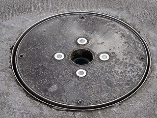 Metal manhole cover in urban setting, textured surface with circular indentations.