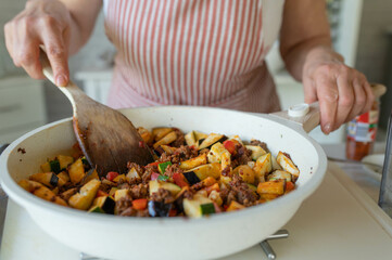Woman preparing healthy pan dish with mediterranen vegetables and minced meat in a frying pan